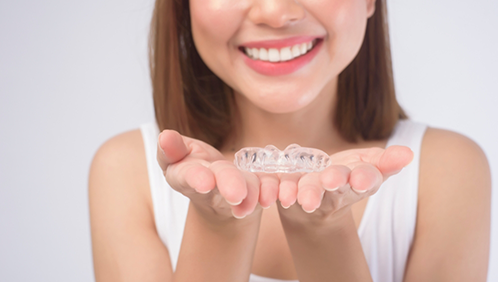 Smiling woman holding two clear aligners in her open palms