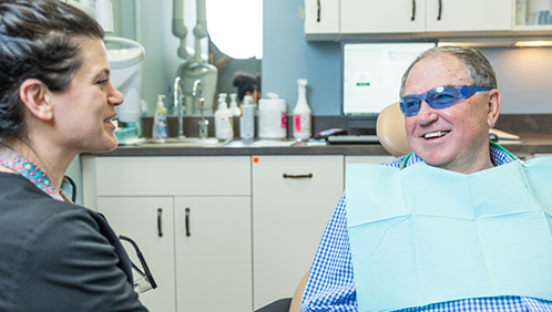 Older man in the dental chair smiling at a dental team member