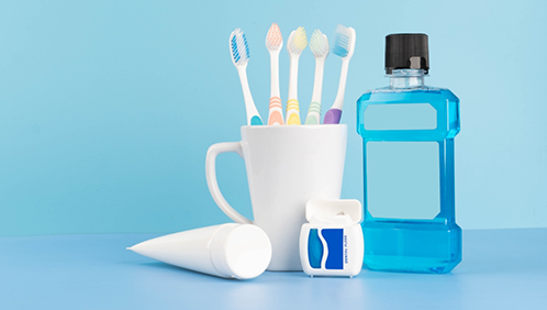 Cup contianing several toothbrushes next to a bottle of mouthwash, a tube of toothpaste, and dental floss
