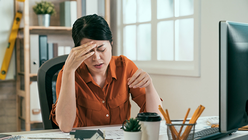 Woman at an office desk rubbing her temples in pain