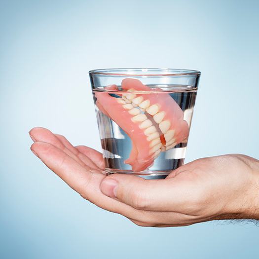 Full set of dentures in glass of clear fluid in the palm of a hand