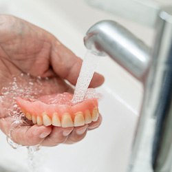 Older hand holding dentures under running water