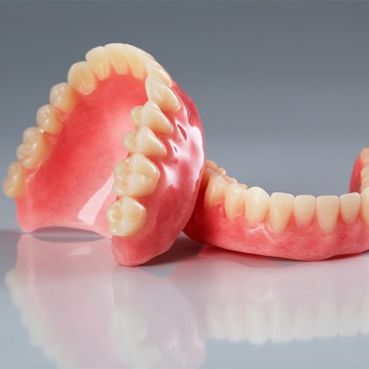 Full set of upper and lower dentures resting on each other on a reflective off-white surface and background