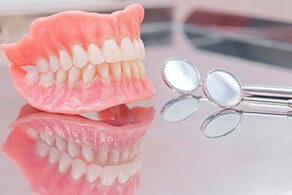 A full set of dentures on a reflective metallic tray next to a dental mirror