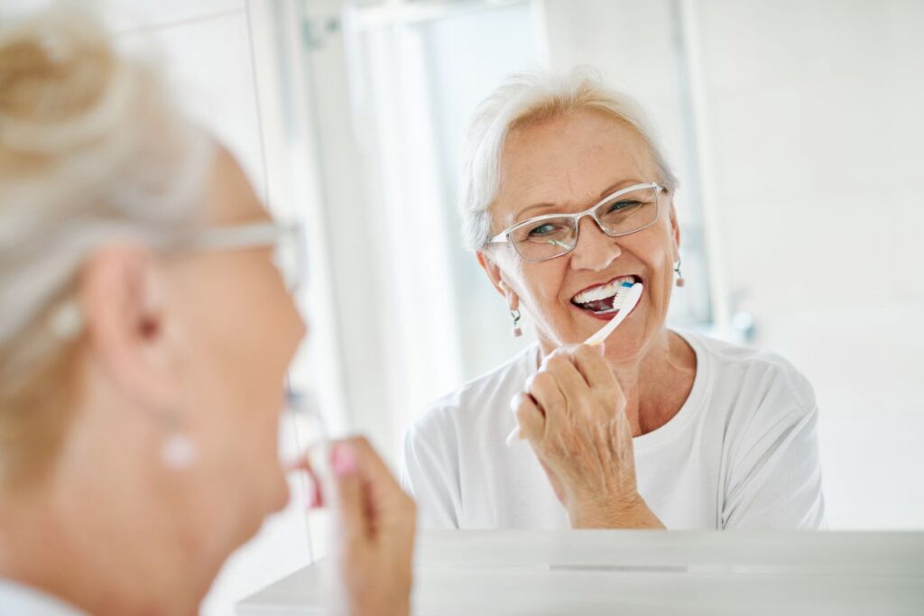 A woman brushing her teeth in the mirror.